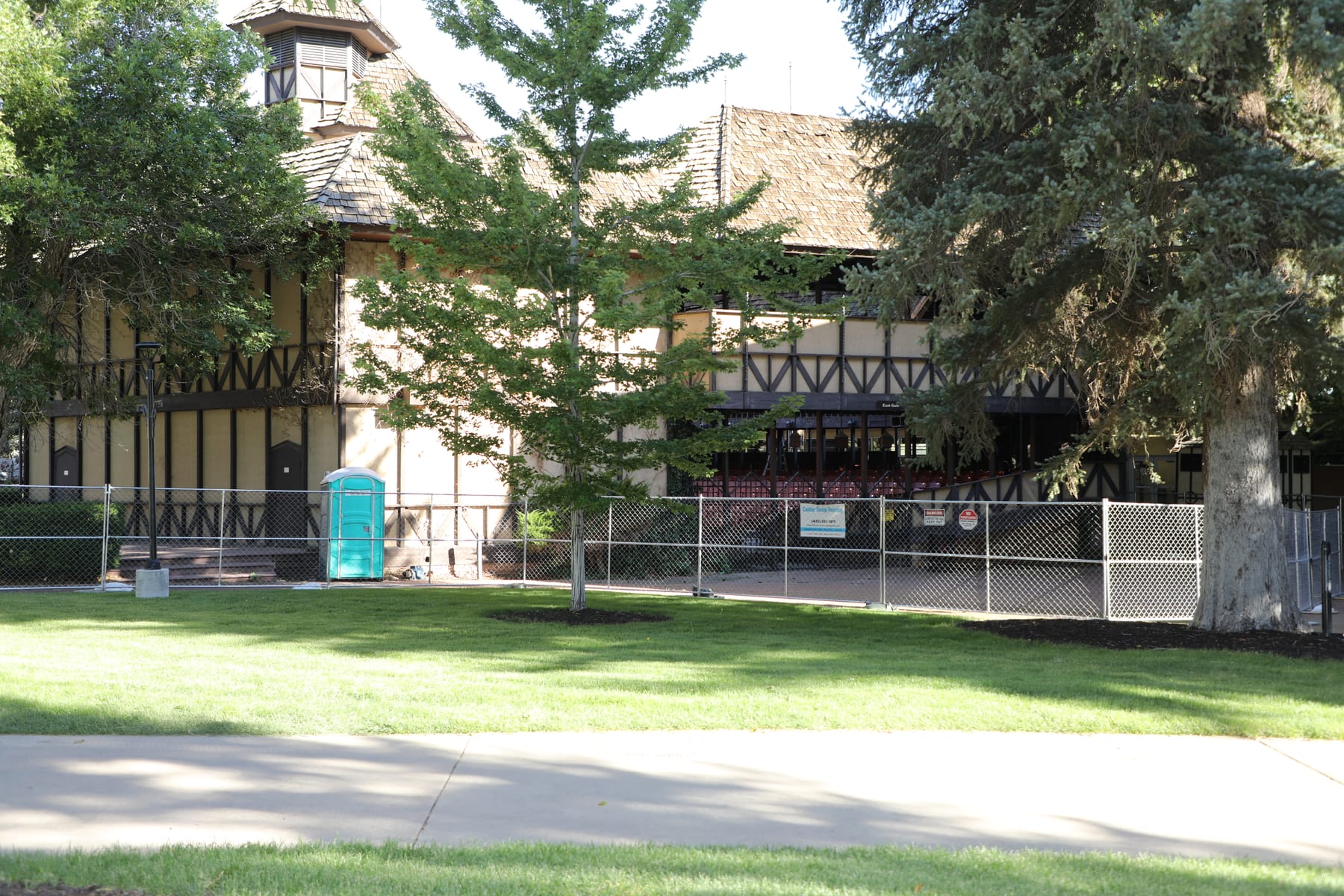 Temporary chain link fence on stands enclosing a work area on the Southern Utah University campus, set on mown lawn beside the Adams Theatre